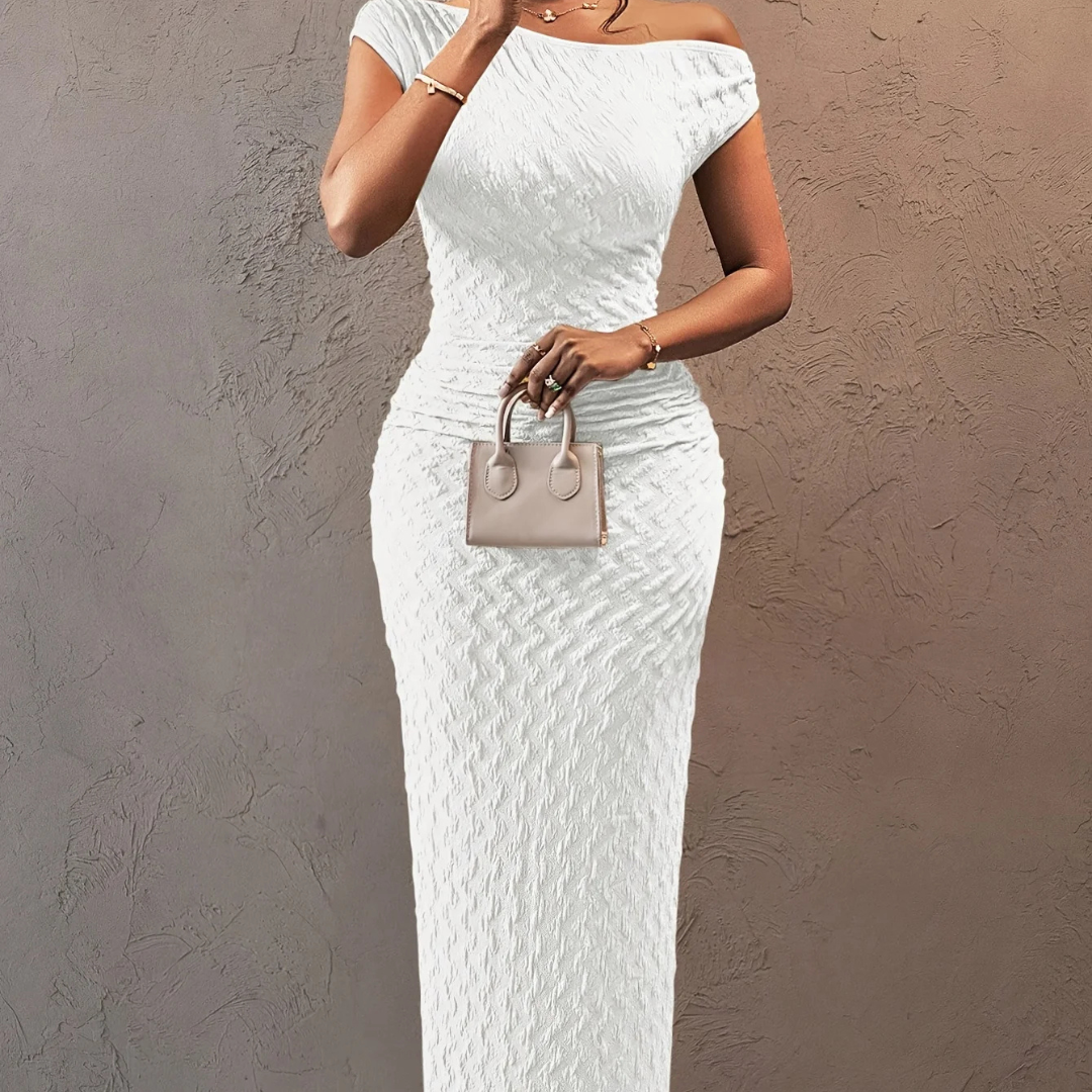 Woman wearing a white lace dress holding a small handbag against a beige wall.