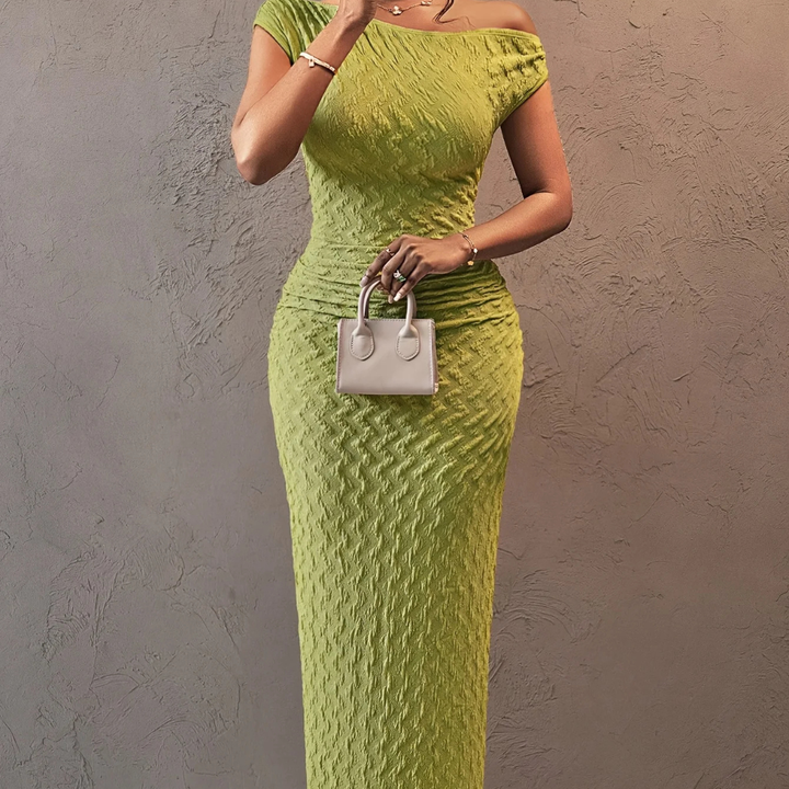Woman wearing a green dress holding a white handbag against a gray wall