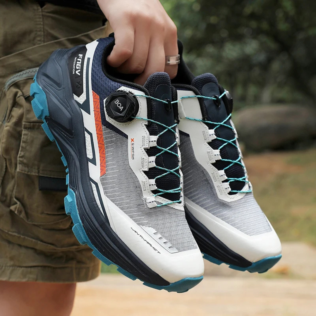 Person holding a pair of dark blue running shoes with a blurred outdoor background