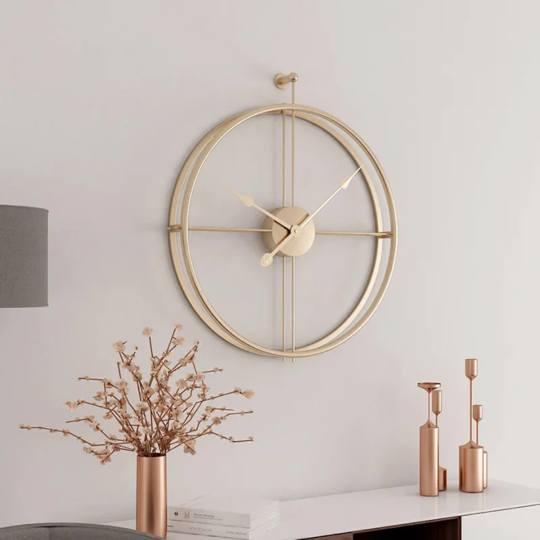 Gold Aurelle Modern Wall Clock on a white wall with decorative vases and branches below.