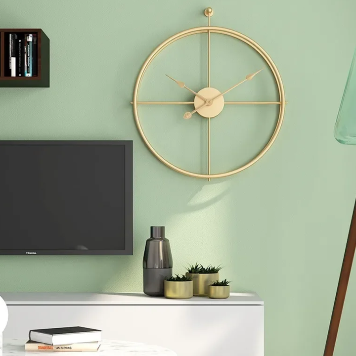 Gold Aurelle Modern Wall Clock on a green wall with a TV and decorative items below.