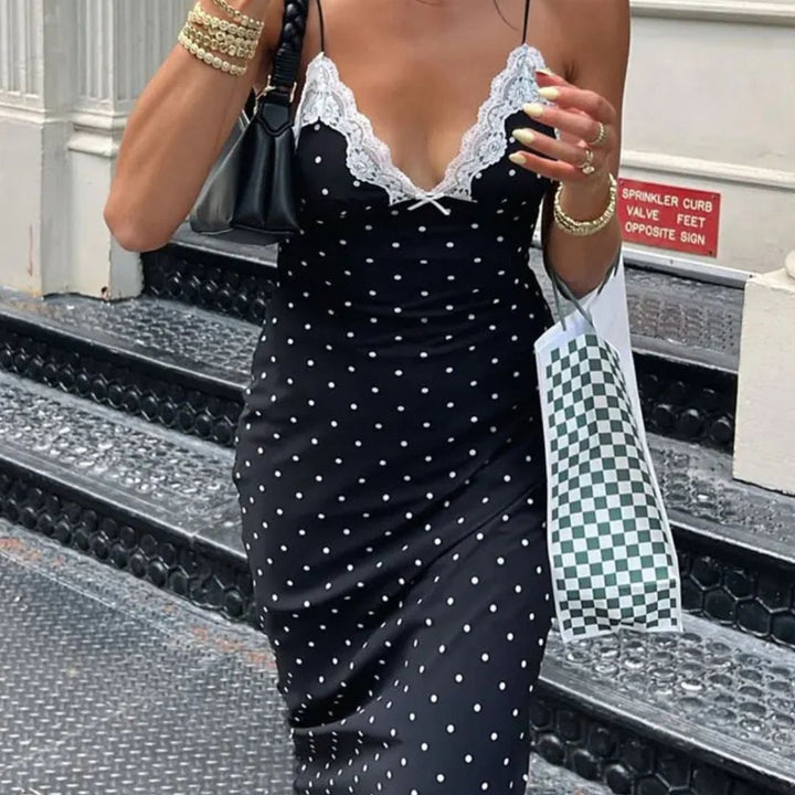 Woman in a black polka dot dress with lace details standing on steps.