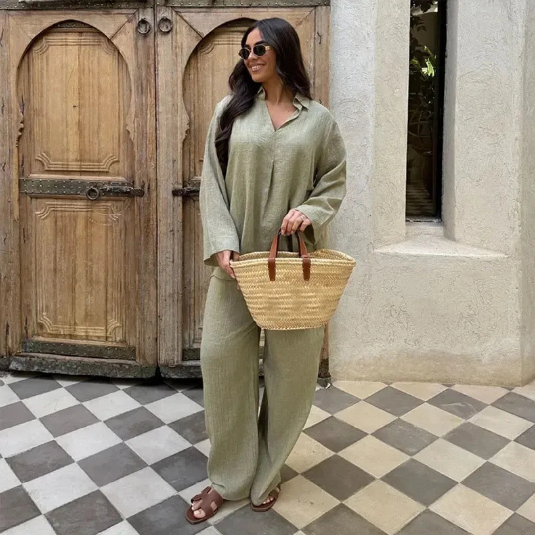 Woman in a Green Celeste Minimal Power Set outfit holding a straw bag in front of a wooden door.