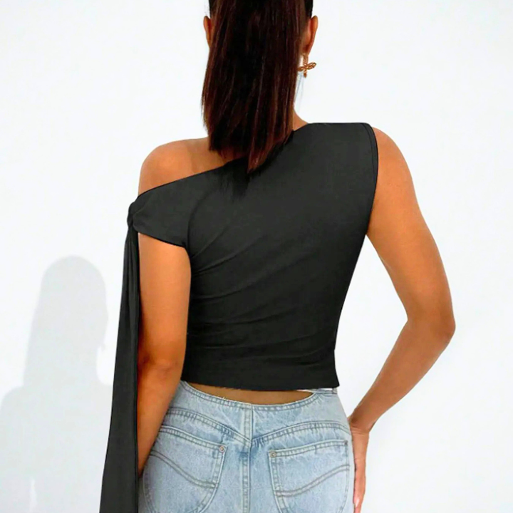 Person wearing a black one-shoulder top and light blue jeans on a white background