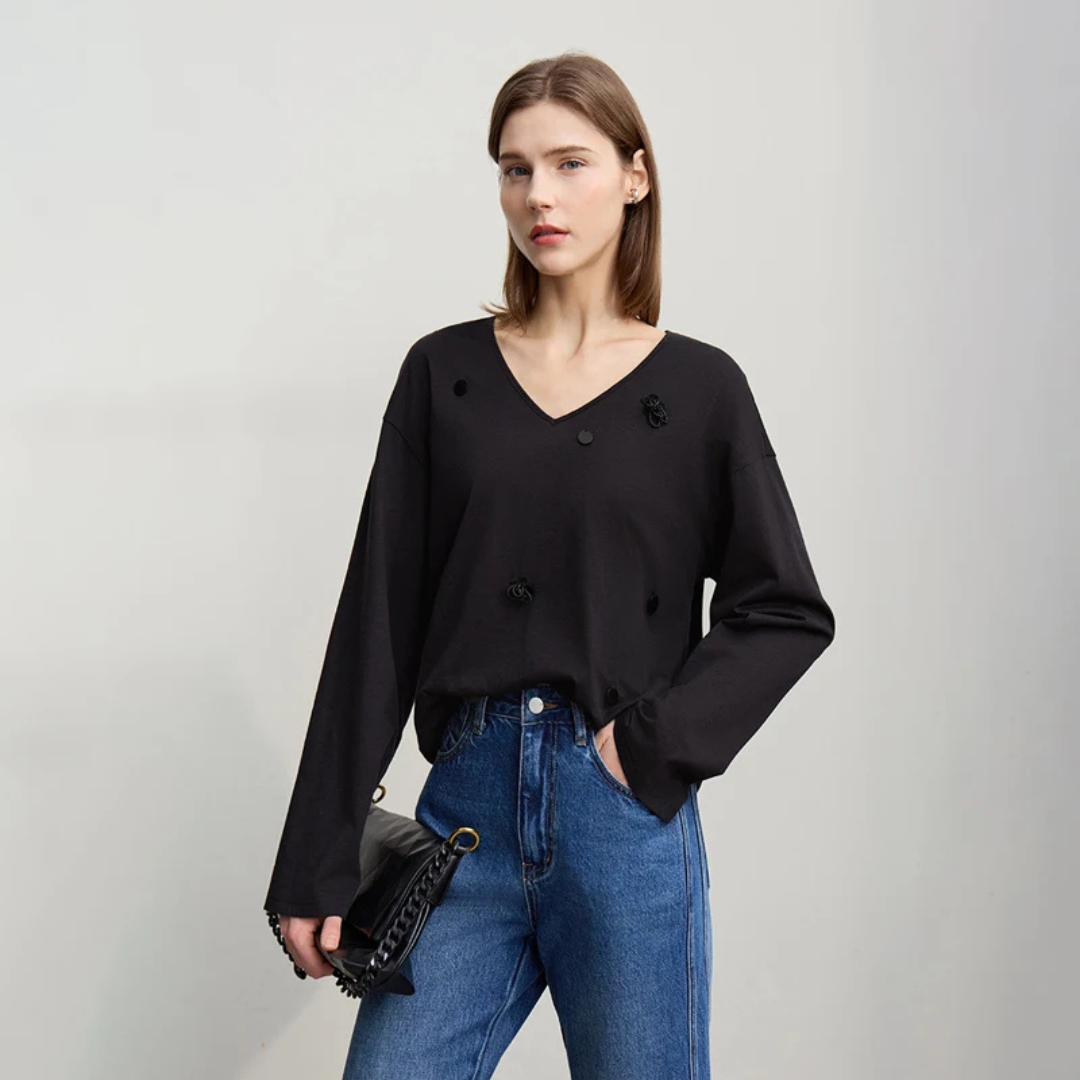 Woman wearing a black top and blue jeans holding a black handbag on a light gray background