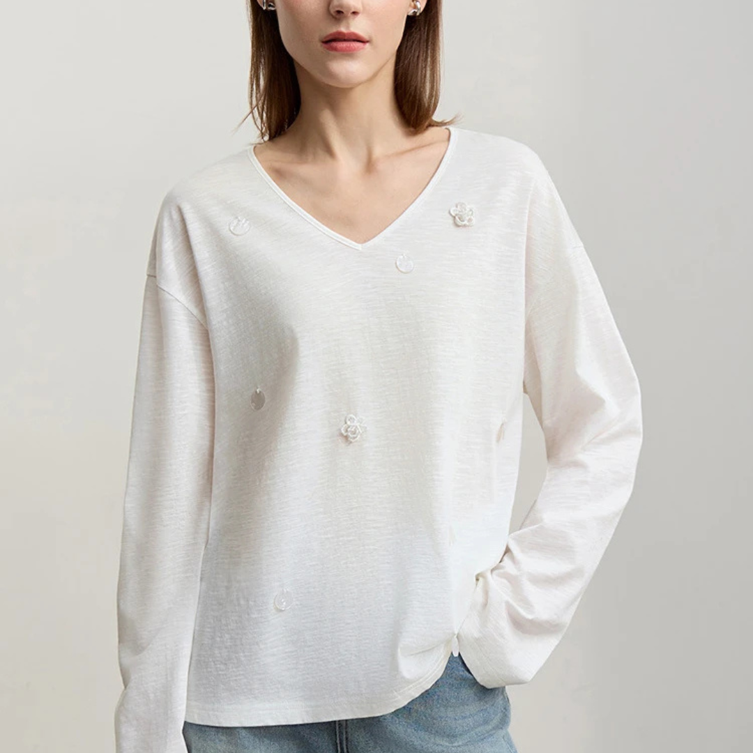 Woman wearing a beige long-sleeve shirt with decorative buttons on a plain background