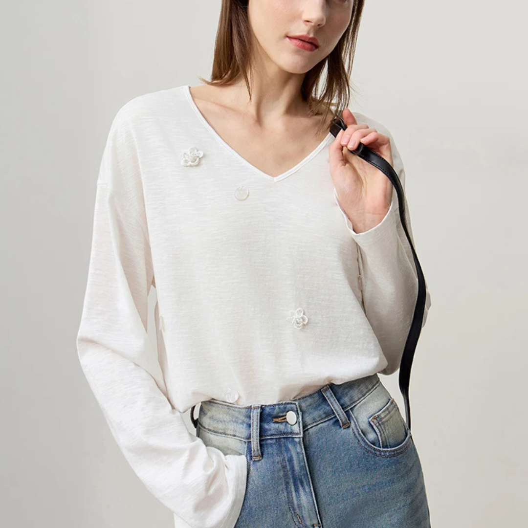 Woman wearing a beige long-sleeve top and blue jeans against a plain background
