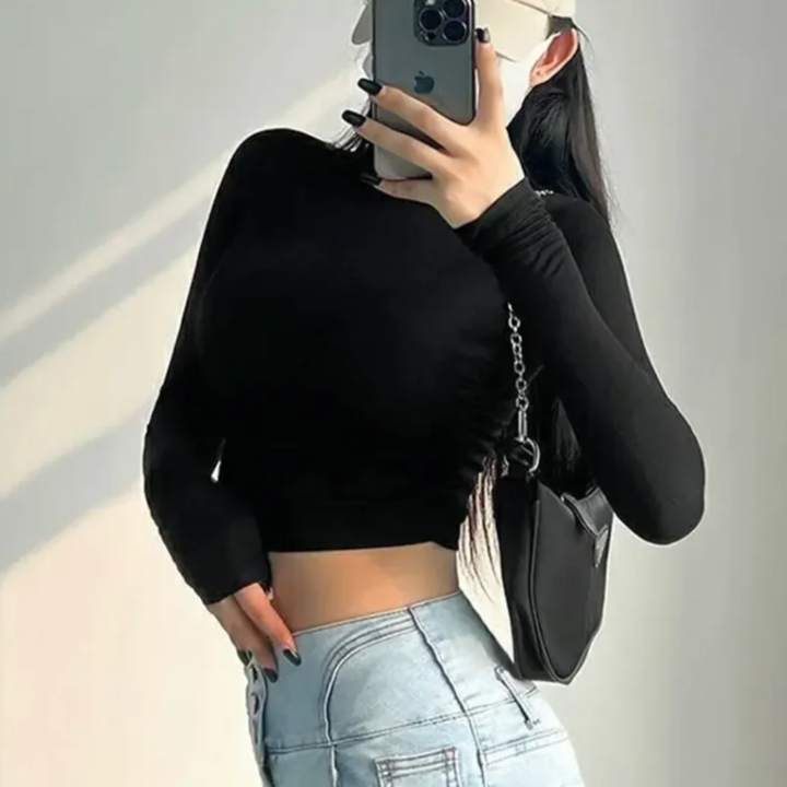 Person wearing a black crop top and light blue jeans, holding a phone.