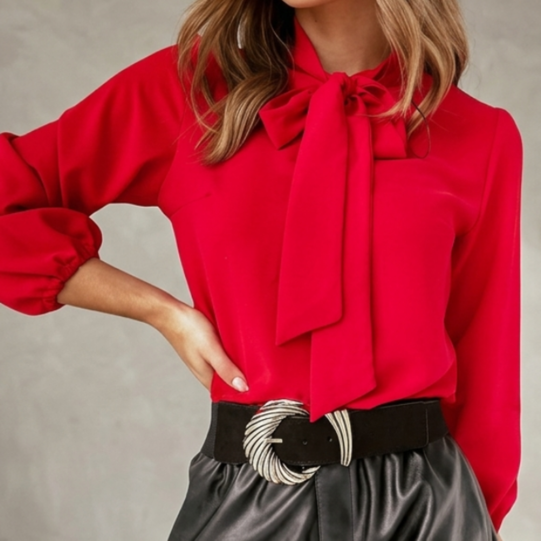 Woman wearing a red blouse with a bow tie and black shorts against a neutral background