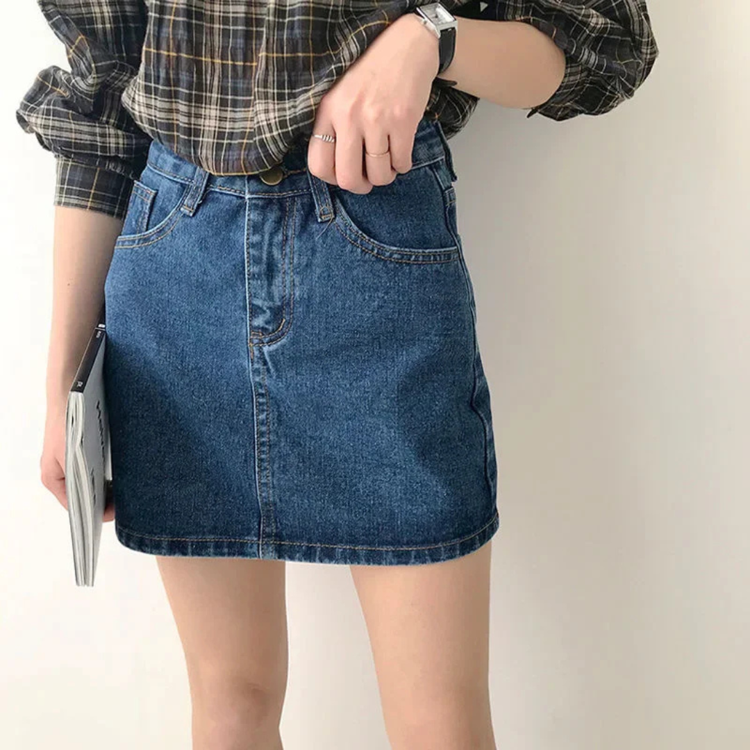 Person wearing a plaid shirt and blue denim skirt holding a book against a plain background