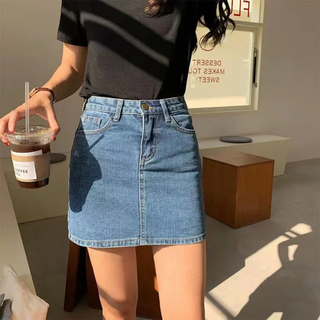 Person wearing a black top and  sky blue denim skirt holding a drink.