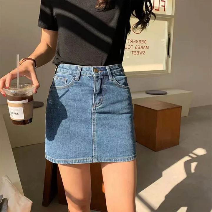 Person wearing a black top and  sky blue denim skirt holding a drink.