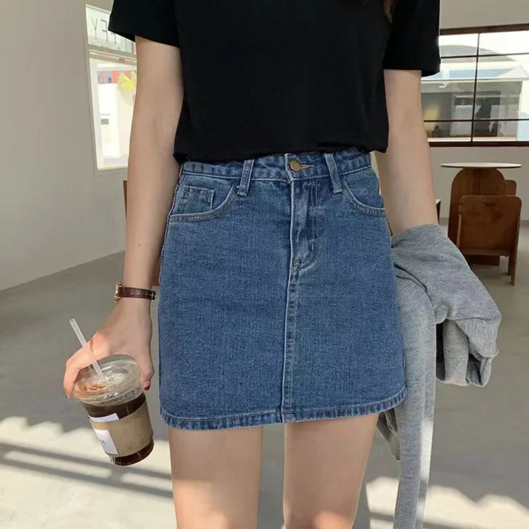 Person wearing a blue denim skirt and black top, holding a drink.