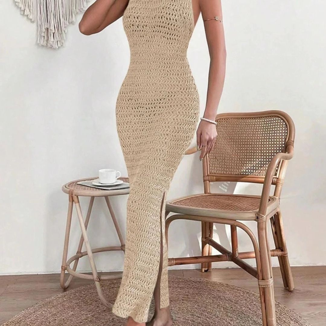 Person wearing a beige crochet dress standing next to a wicker chair and small table.