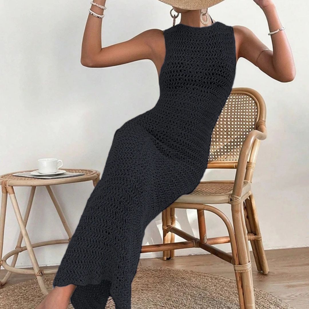 Person wearing a black crochet dress sitting on a wicker chair.