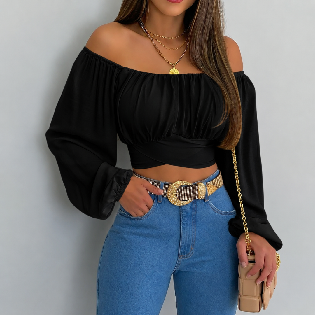 Woman wearing a black off-shoulder top and blue jeans with a gold belt, holding a beige clutch.