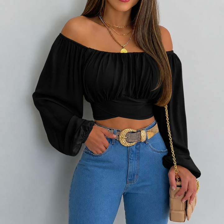 Woman wearing a black off-shoulder top and blue jeans with a gold belt, holding a beige clutch.