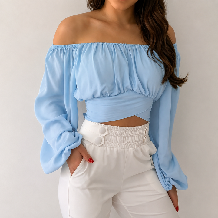 Woman wearing a light blue off-shoulder top and white pants against a neutral background