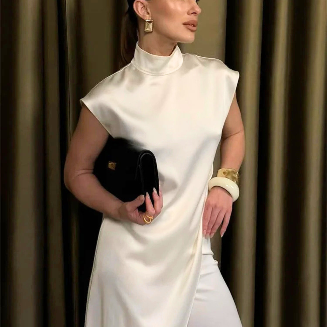 Woman in a white dress holding a black clutch against a curtain background