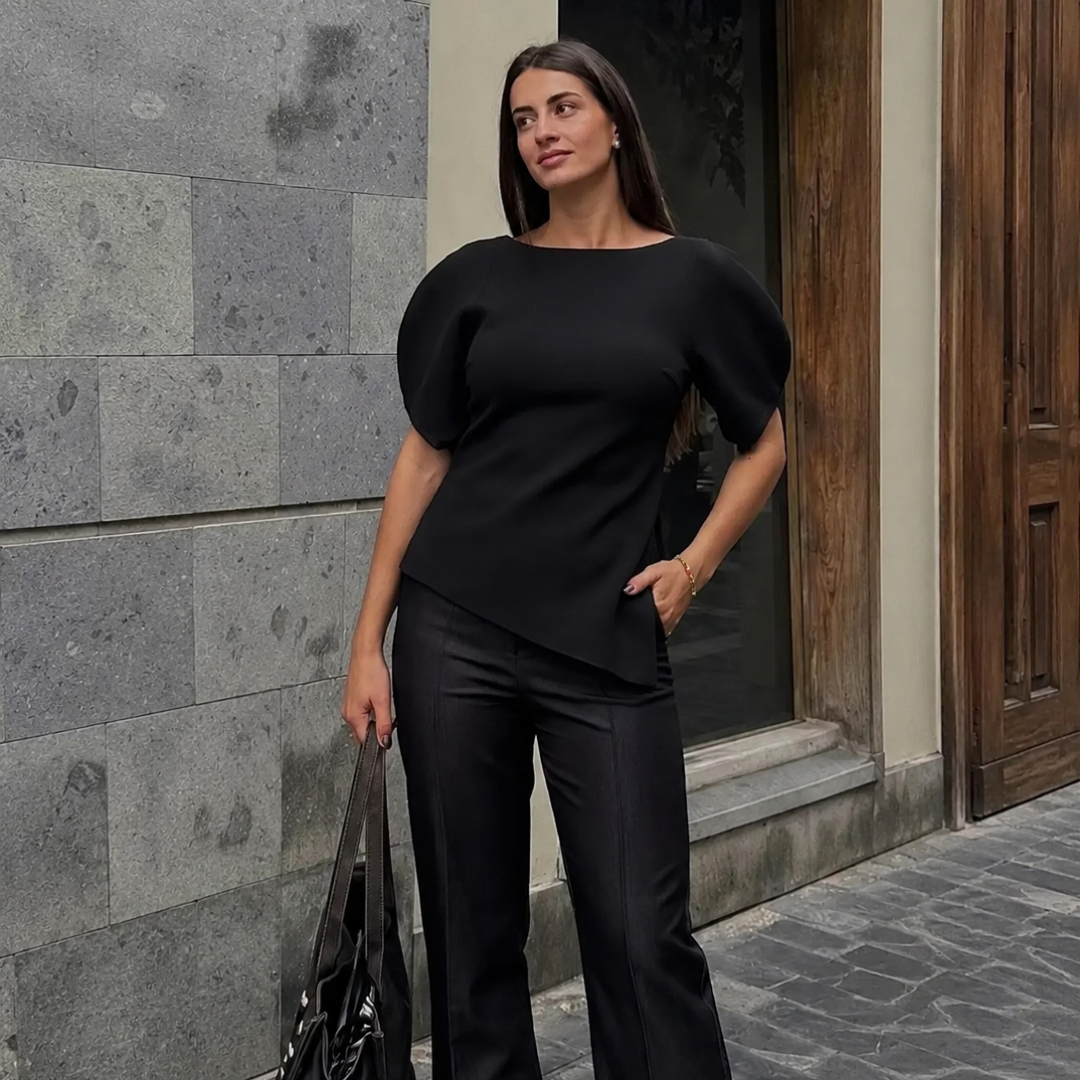 Woman in a black outfit standing against a stone wall.