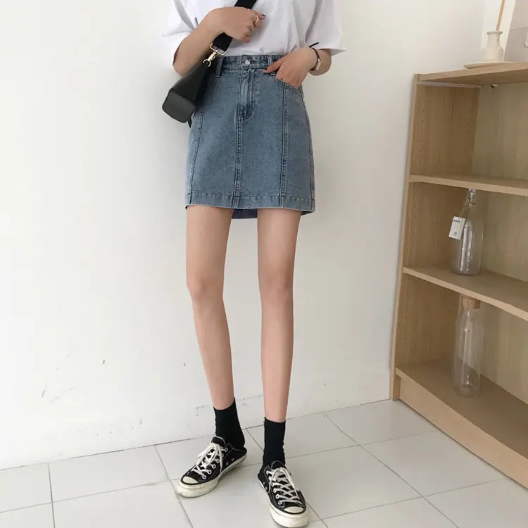 Person wearing a blue denim skirt and black sneakers in a minimalistic room.