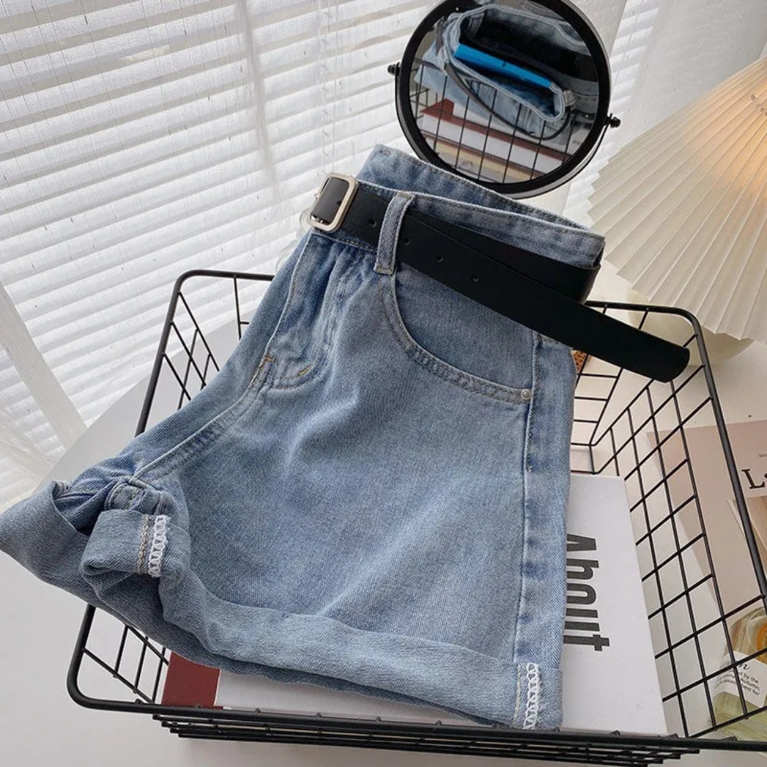 Folded Outlaw Muse Wide-Leg Sky Blue Denim Shorts with a belt on top of a magazine