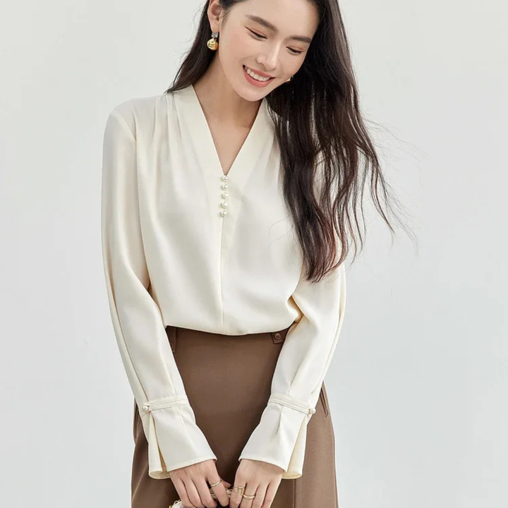 Woman wearing a beige blouse and brown pants on a light gray background