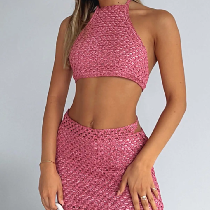 Person wearing a pink crochet top and skirt set on a plain background
