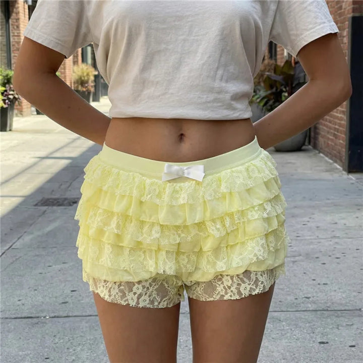 Person wearing a light gray crop top and yellow lace shorts on a sidewalk.