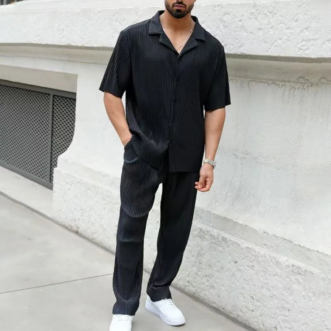 Man wearing a black striped shirt and pants standing against a white wall.
