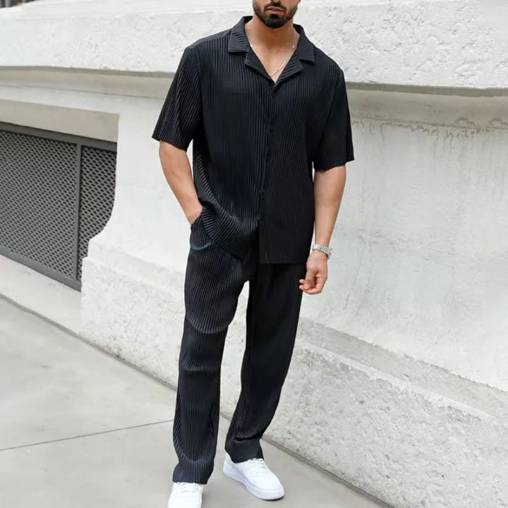 Man wearing a black striped shirt and pants standing against a white wall.
