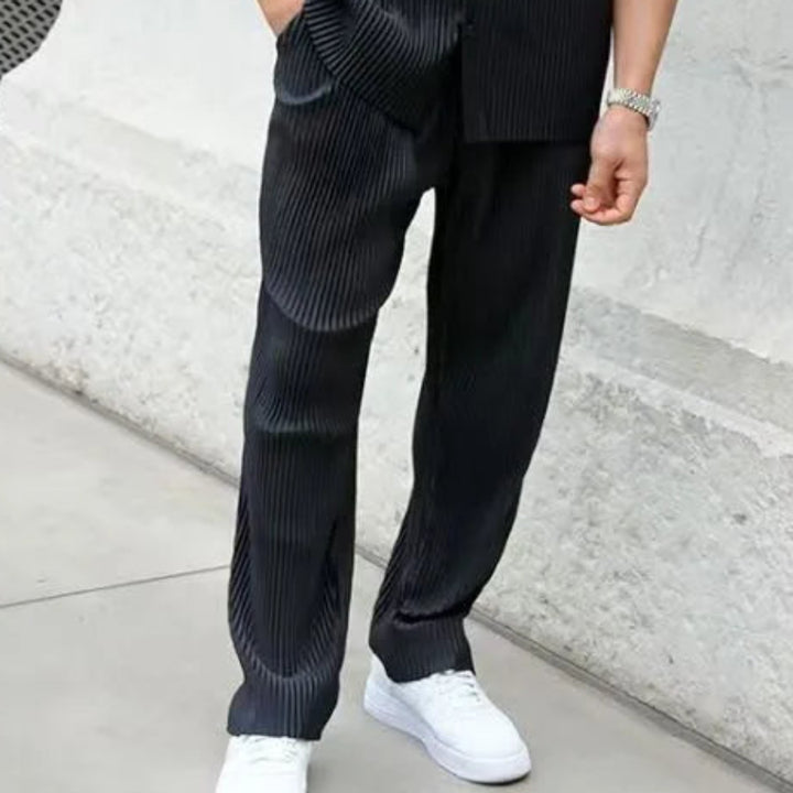 Man wearing a black striped pants standing against a white wall.