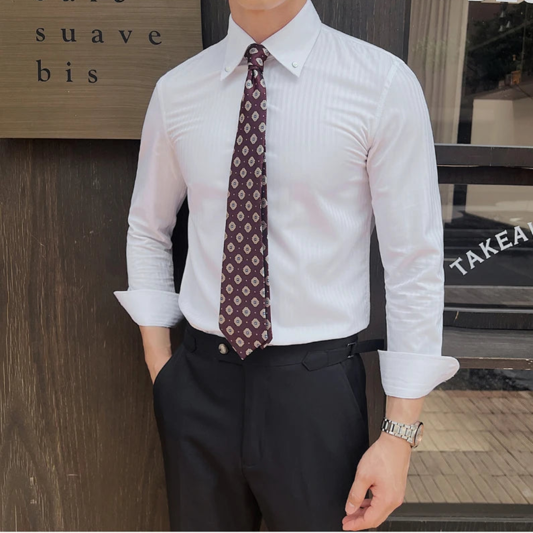 Person wearing a white rolled-up sleeves, a patterned tie, and dark pants in front of a wooden wall.