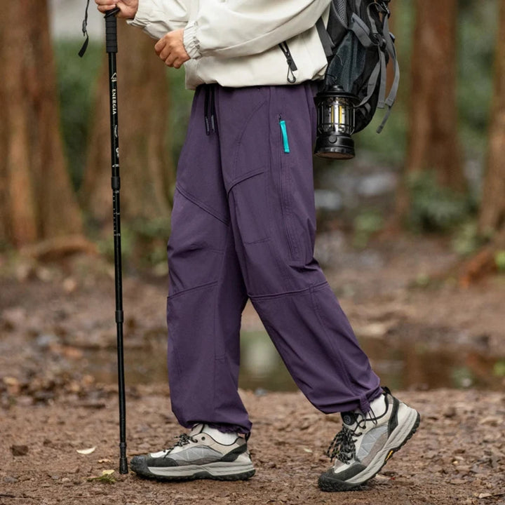 Person wearing purple hiking pants with a backpack and walking stick in a forest setting