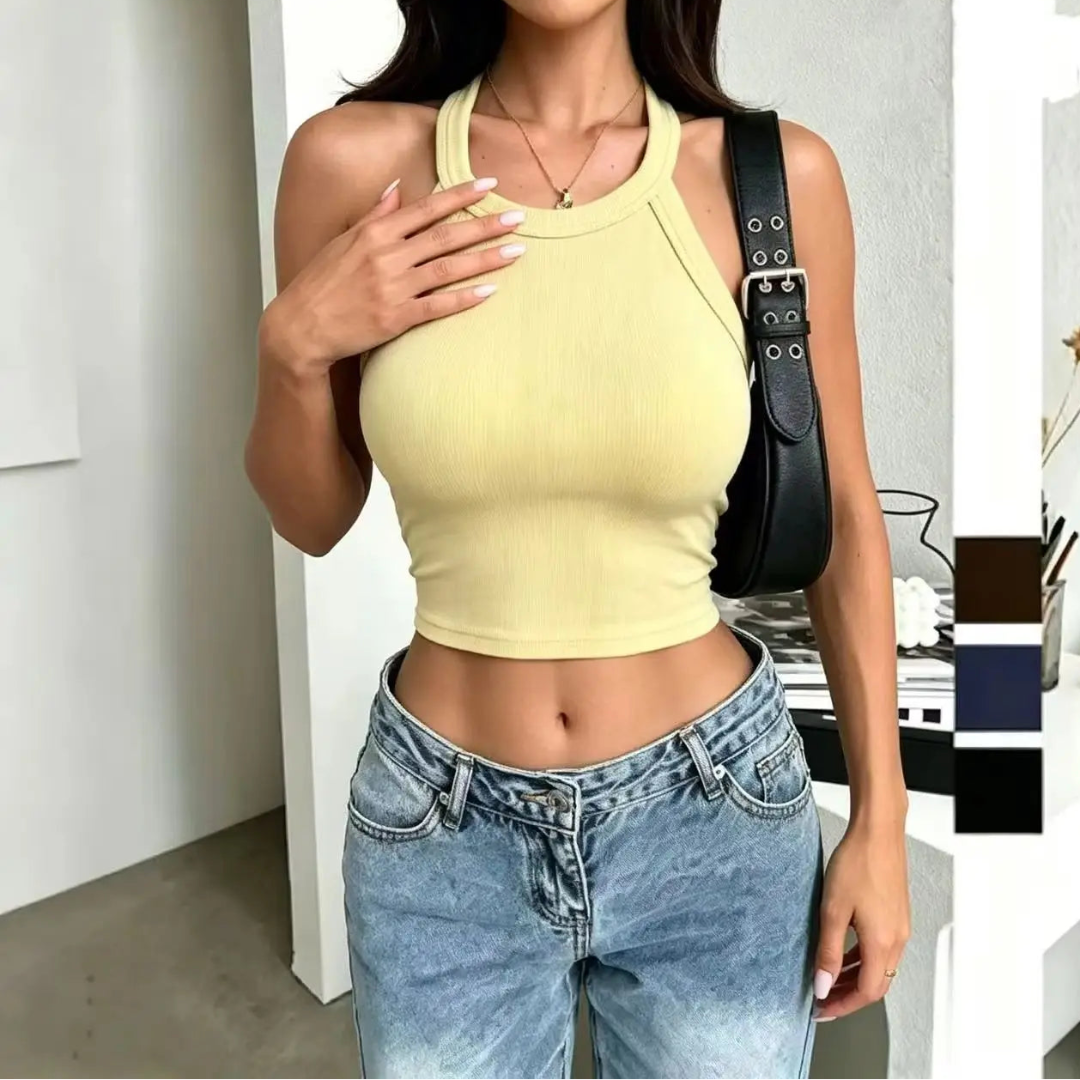 Woman wearing a yellow crop top and blue jeans indoors.