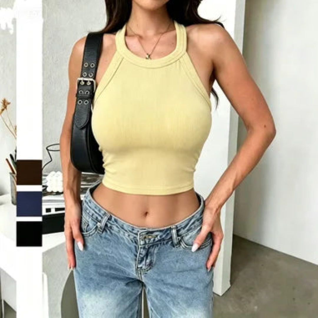 Woman wearing a yellow crop top and blue jeans with a black bag over her shoulder.