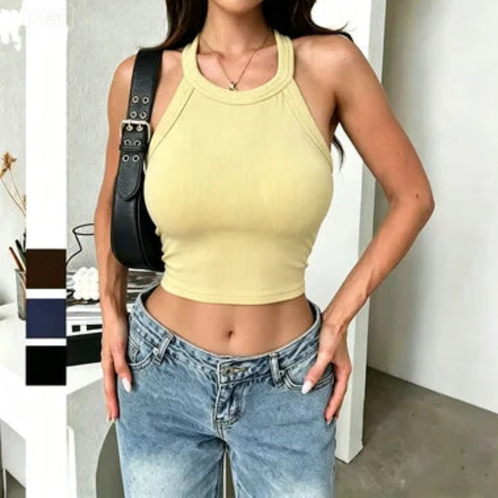 Woman wearing a yellow crop top and blue jeans with a black bag over her shoulder.
