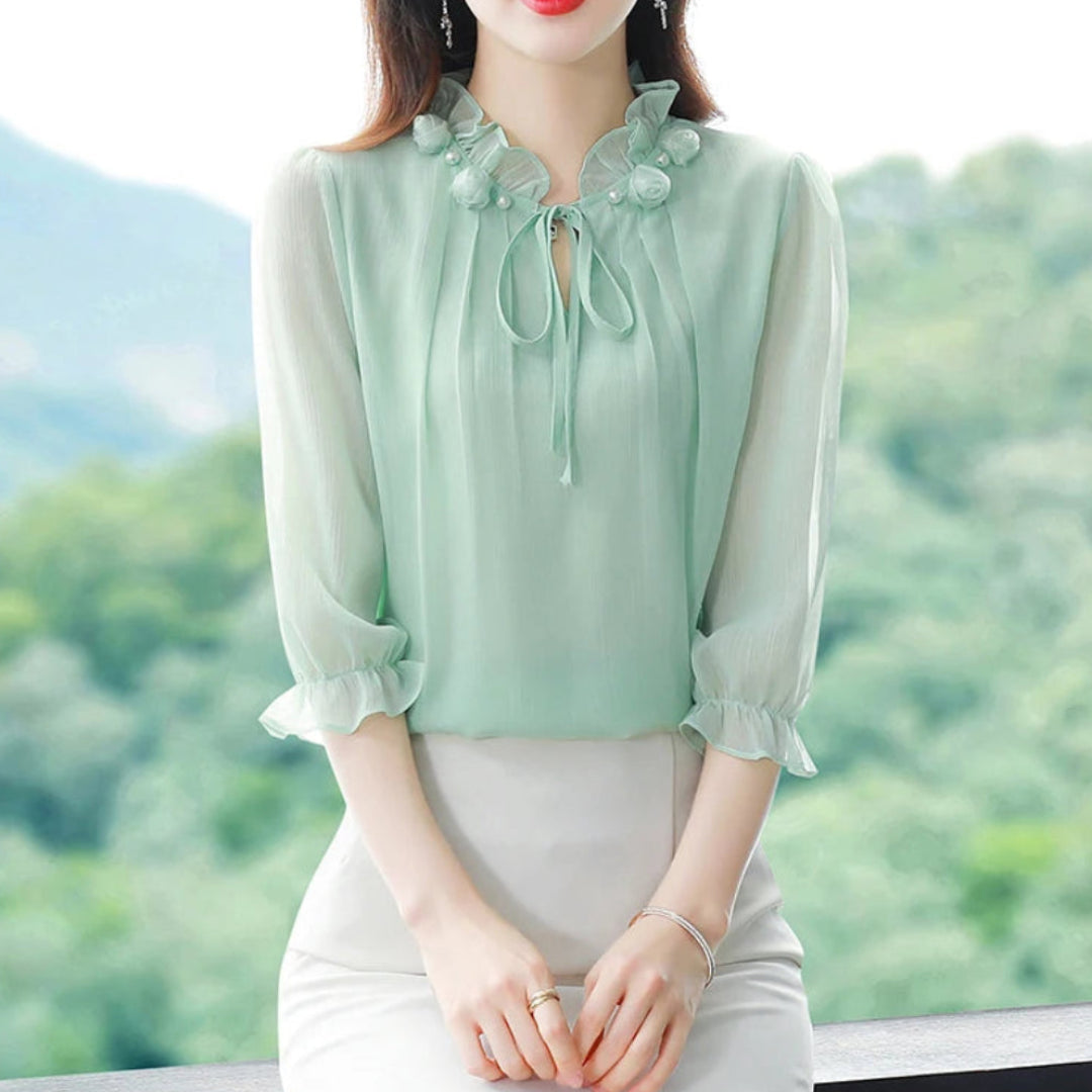 Woman wearing a green blouse with floral details against a blurred natural background