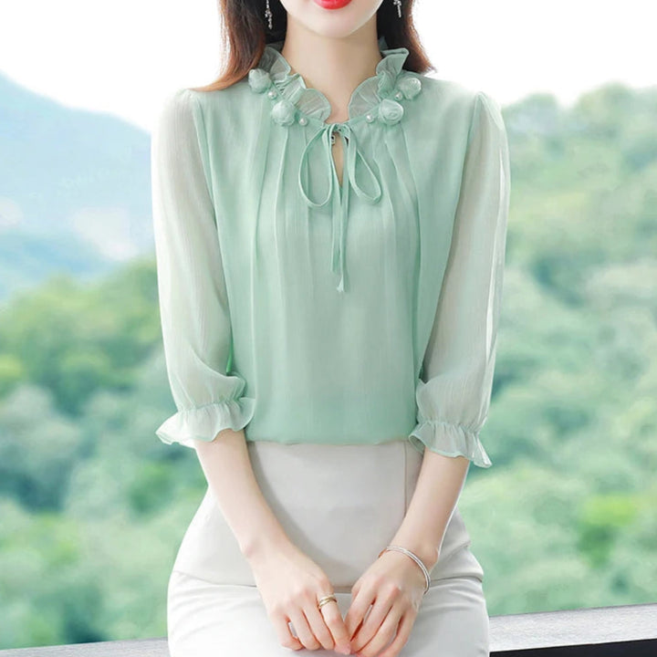 Woman wearing a green blouse with floral details against a blurred natural background