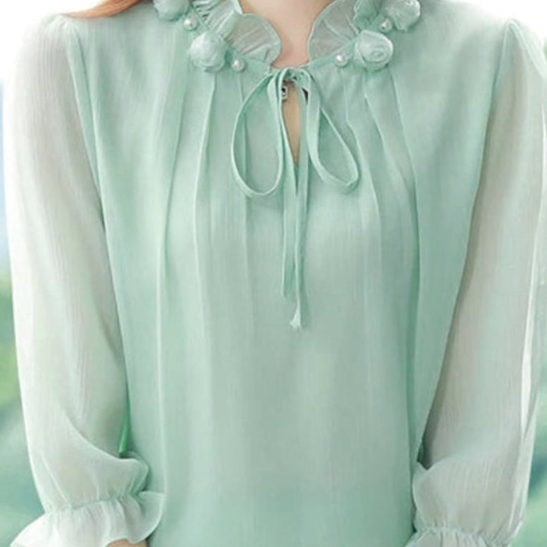 Woman wearing a green blouse with floral details against a blurred natural background