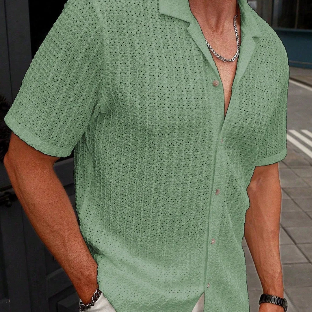 Person wearing a green patterned shirt with a blurred background