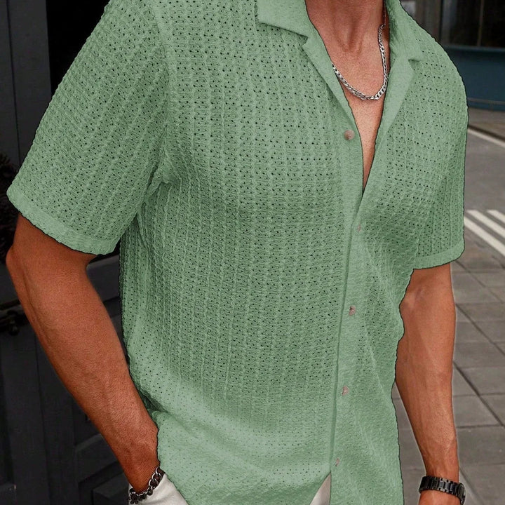 Person wearing a green patterned shirt with a blurred background