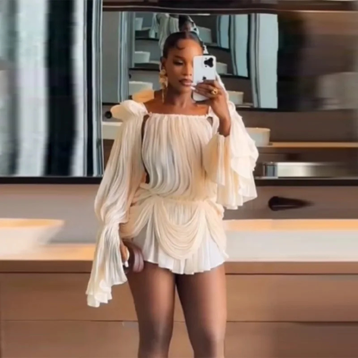 Woman taking a mirror selfie wearing a white off-shoulder outfit in a modern kitchen.