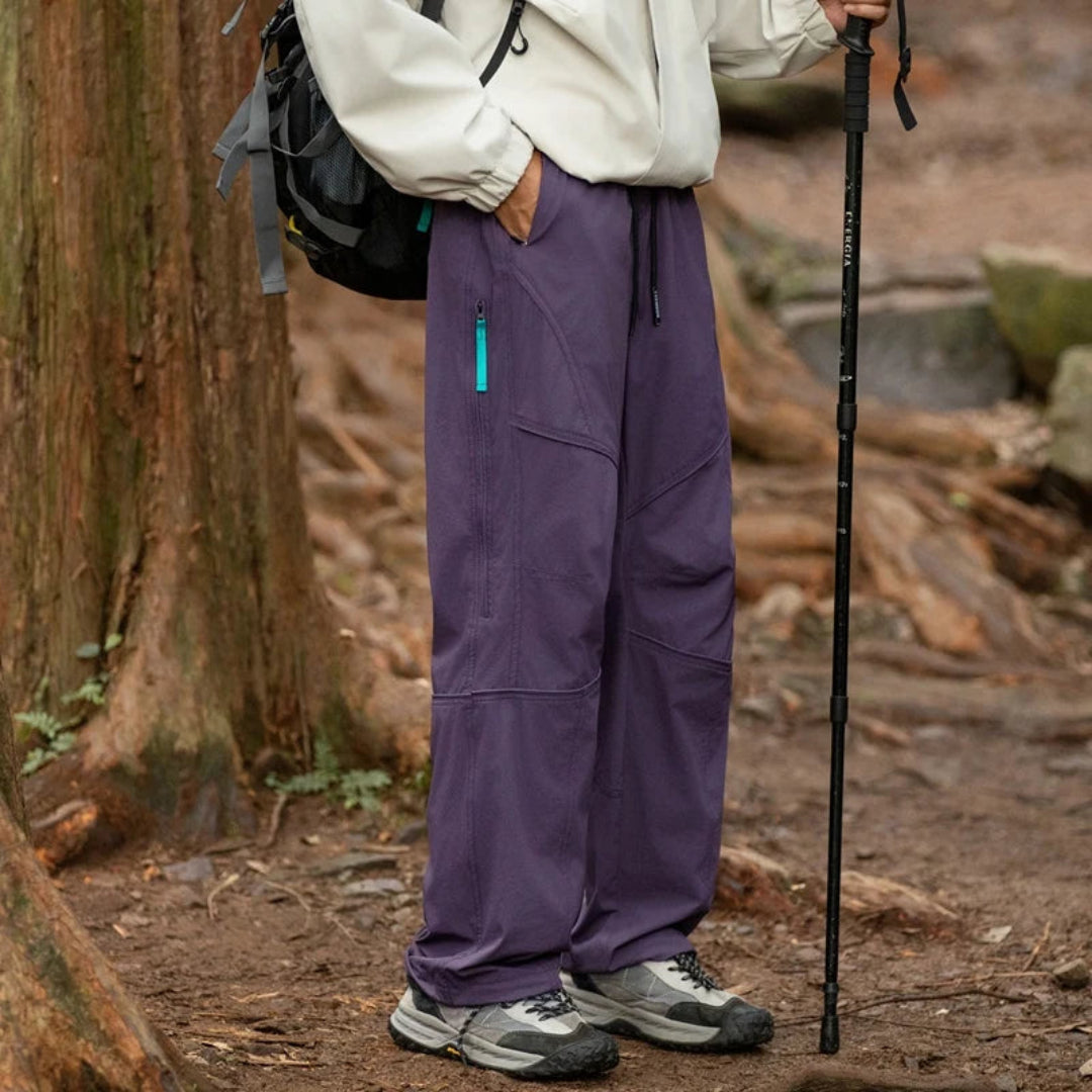 Person wearing purple pants and a white jacket with a backpack and walking stick in a forest setting