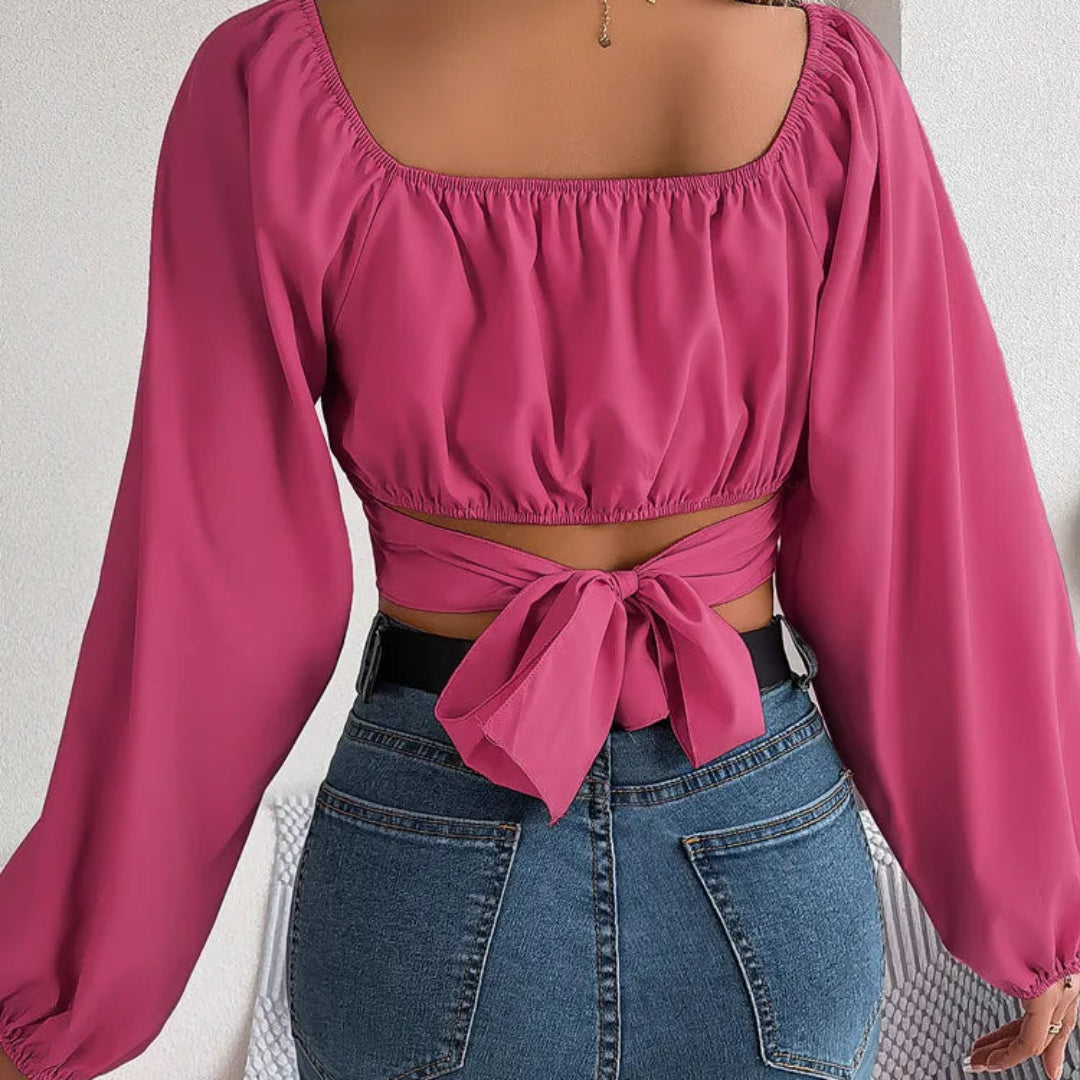 Person wearing a pink blouse with long sleeves and tied waist, paired with blue jeans.