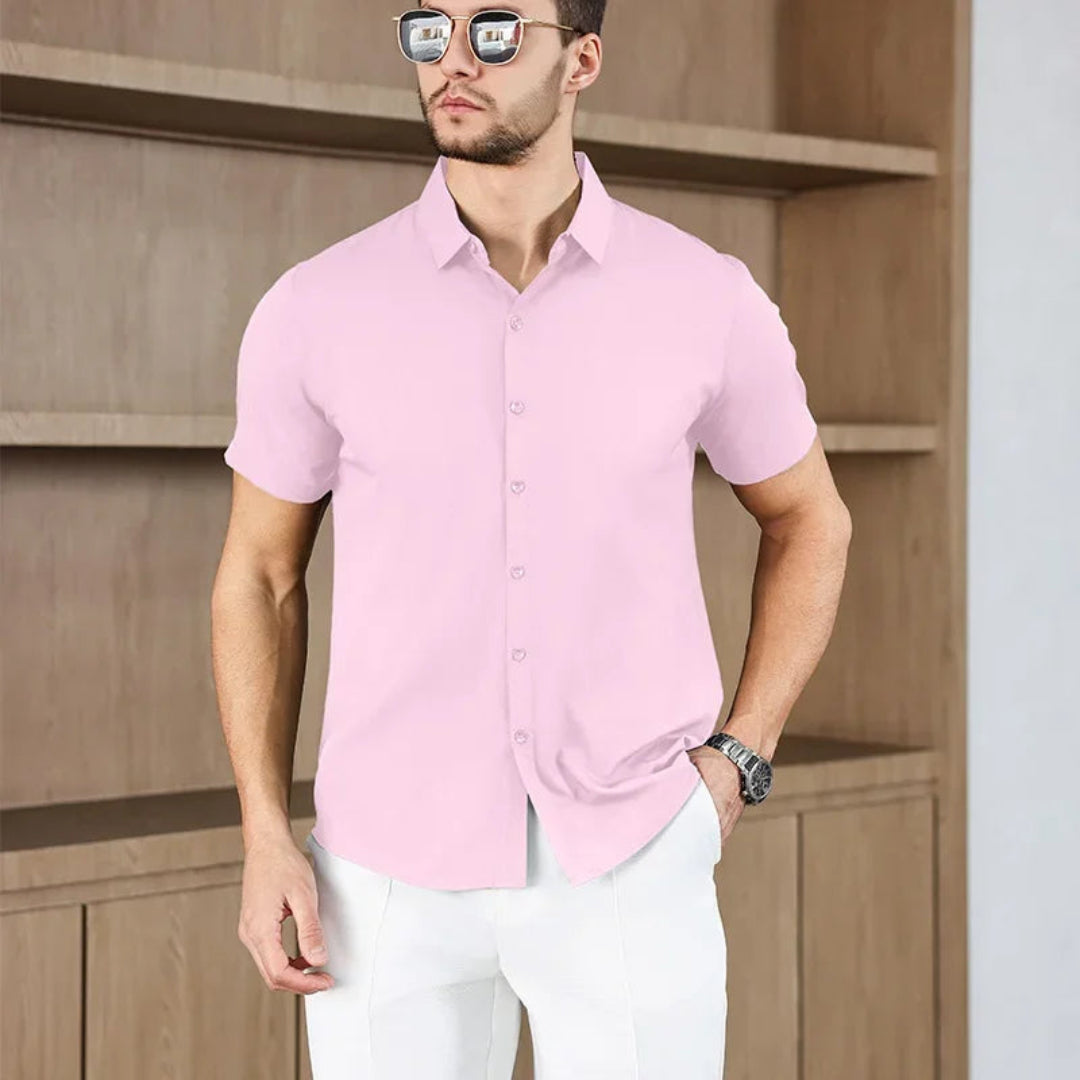 Man wearing a pink short-sleeve shirt and white pants against a wooden background
