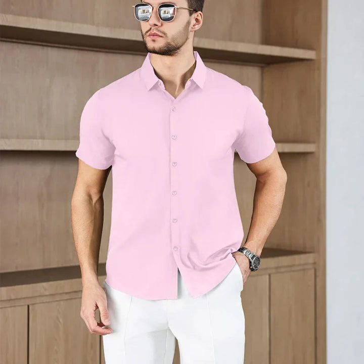 Man wearing a pink short-sleeve shirt and white pants against a wooden background