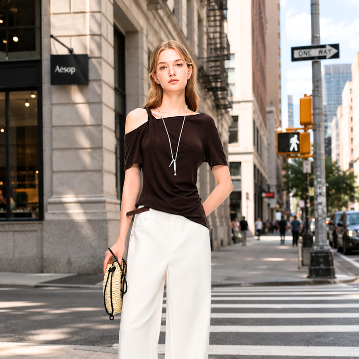 Woman in a brown top and white pants standing on a city street with Aesop store in the background