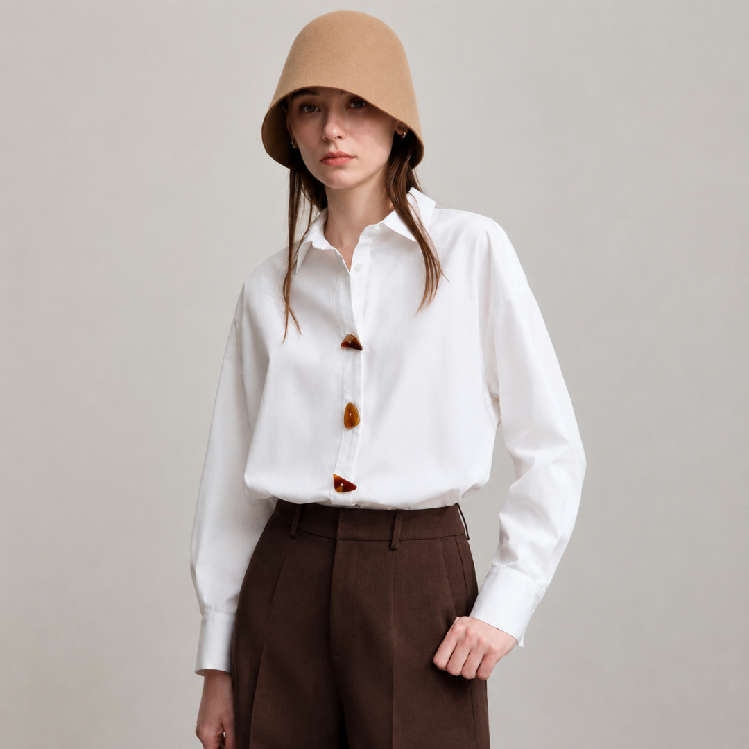 Woman wearing a white shirt with brown buttons and brown hat and pants on a plain background
