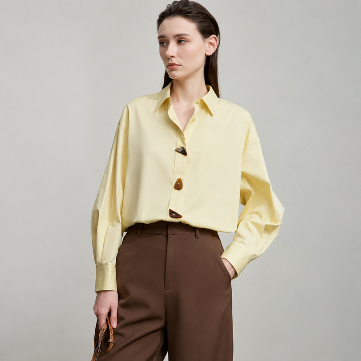 Woman wearing a yellow blouse and brown pants on a gray background